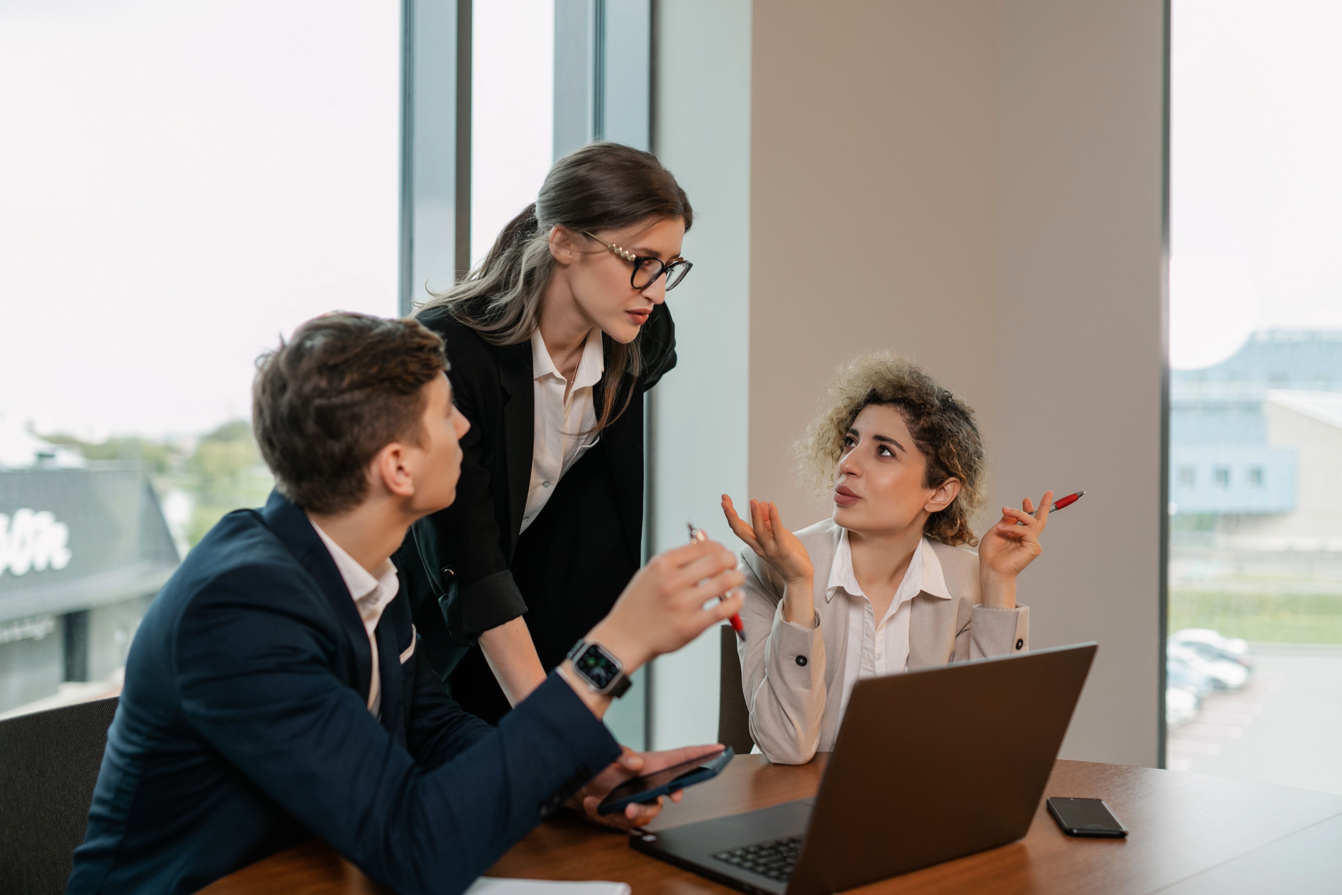 Three people discussing work around a laptop — illustrative photograph